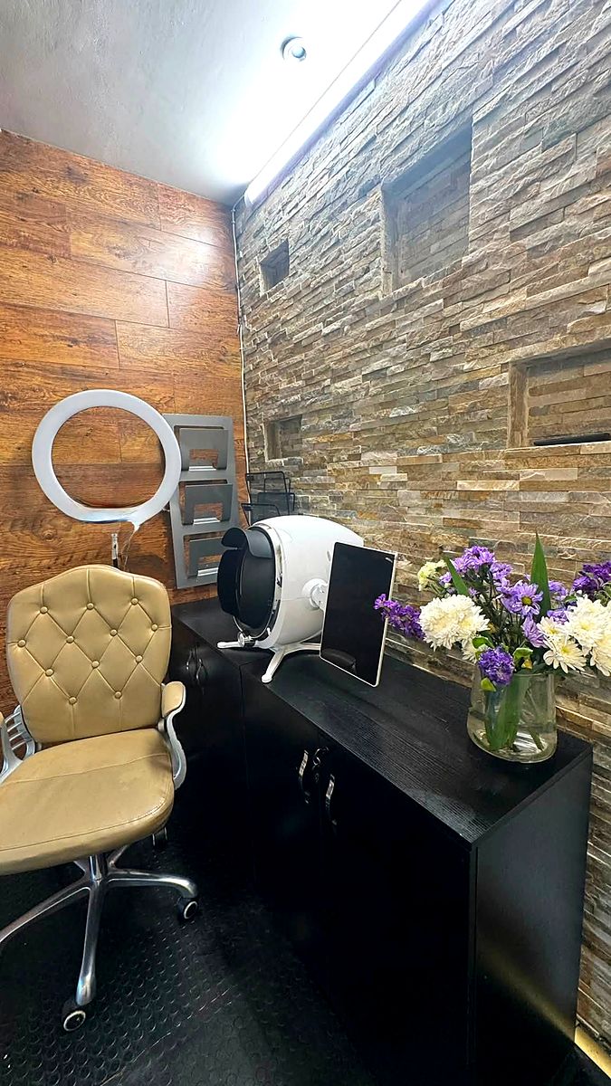 A consultation desk with a ring light and magnifying lamp against a stone wall, with flowers on the counter