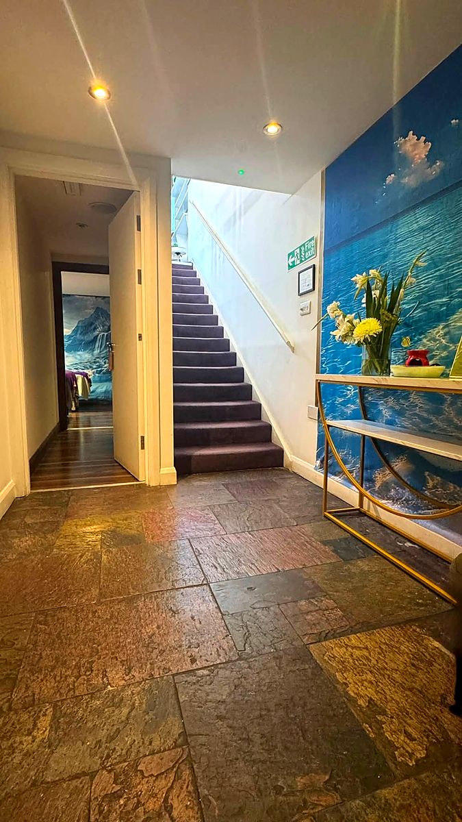 A hallway with a stone floor, a painted sea mural along one wall and stairs leading up