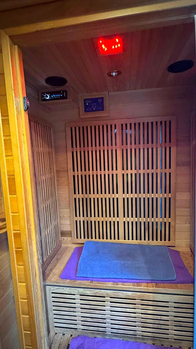 The wooden infrared sauna cabin with its door open, bench inside and a lit control panel