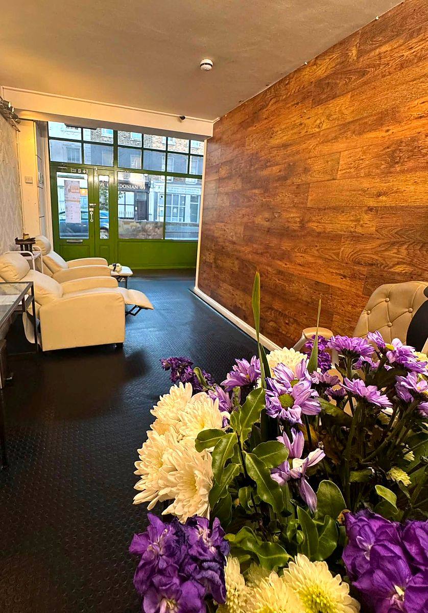 The front pedicure room with white reclining chairs, daylight through the window onto the street, flowers in the foreground