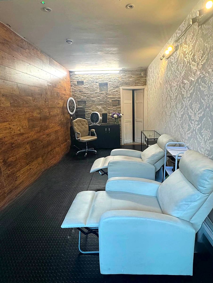 A row of white reclining pedicure chairs along a corridor with stone and wood-panelled walls