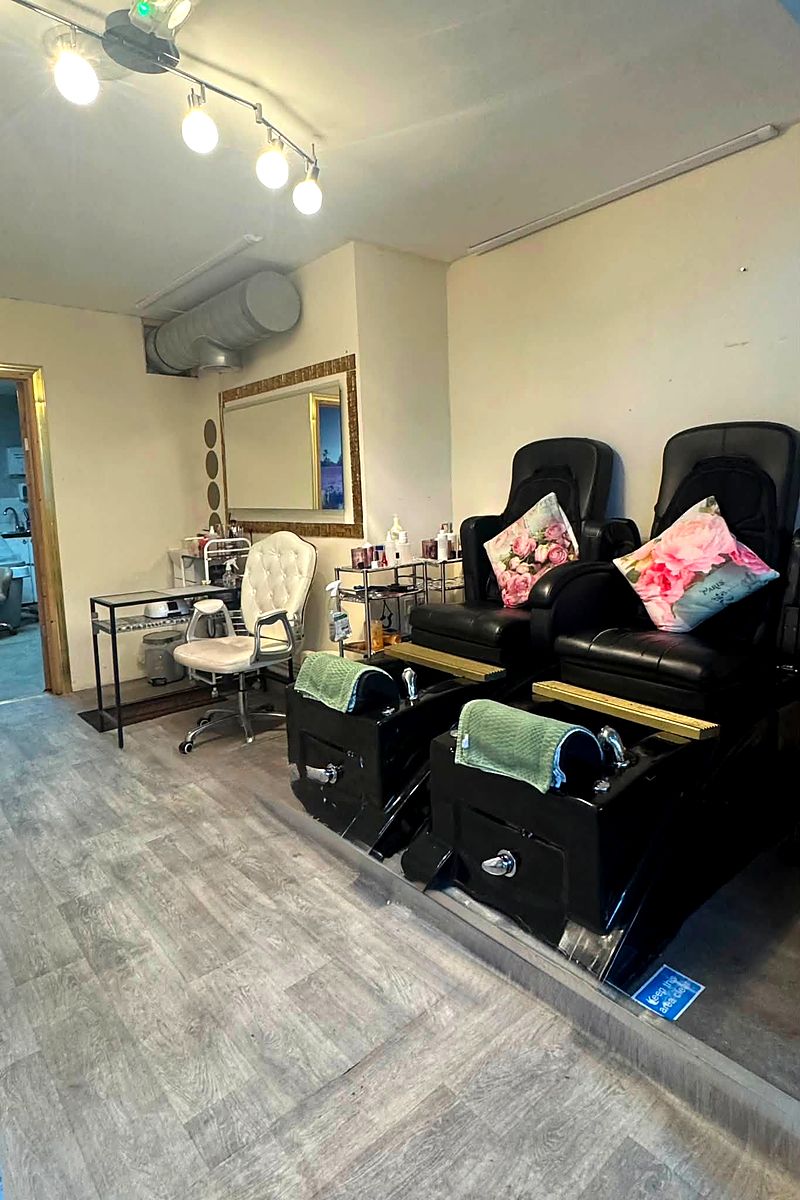 Two black pedicure spa chairs with cushions and green towels, mirrors and a styling station behind