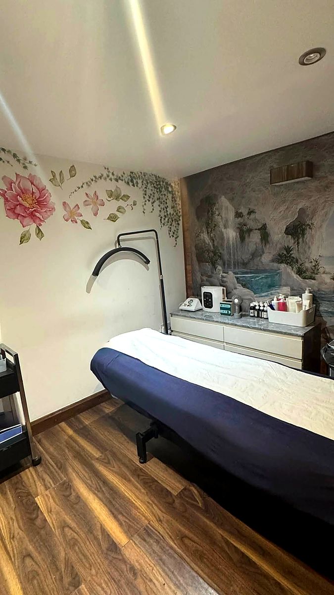 A facial treatment room with a floral wall mural and a product trolley beside the bed