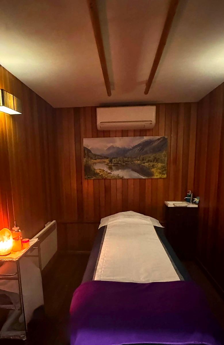 A single treatment room panelled in dark wood with a warm lamp on the side table